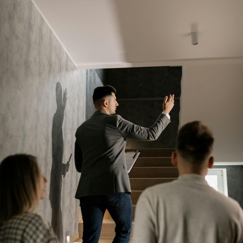 Immobilienmakler führt ein Paar durch ein modernes Treppenhaus bei einer Wohnungsbesichtigung